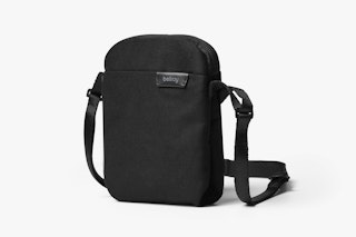 Bellroy City Pouch in black, rectangular with fine fabric, adjustable strap and logo pendant on the front, shown upright on a white background.