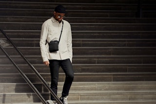 A man carries a black Bellroy City Pouch cross-body bag as he walks down a concrete staircase, highlighting the bag's sleek, hands-free design.