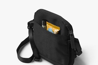 Bellroy City Pouch in melbourne_black with fine_weave texture, outer pocket holding lip balm and snack bar, on white background.