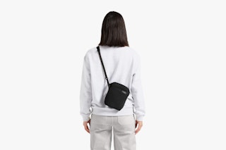 A black Bellroy City Pouch with a textured surface, worn over the shoulder by a person in light gray clothing seen from behind.