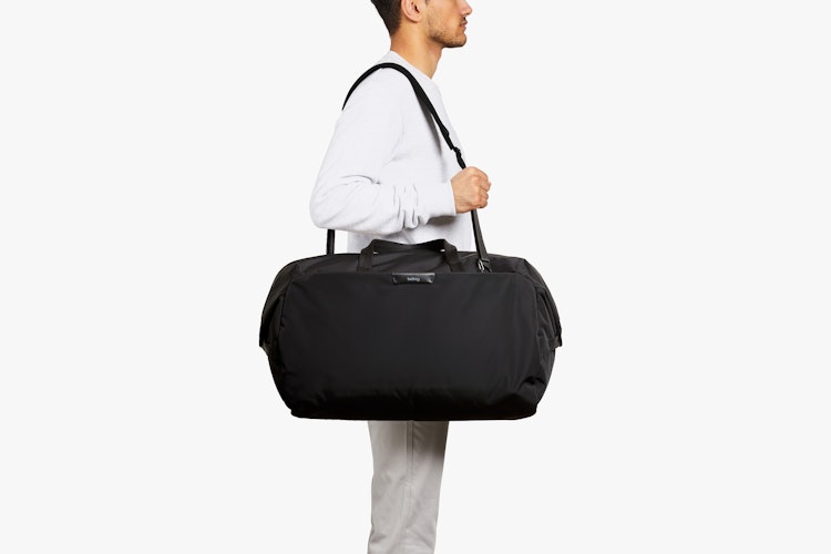 A man carries the black Bellroy Classic Weekender 45L duffel bag, showing the size, handles and straps against a plain white background.
