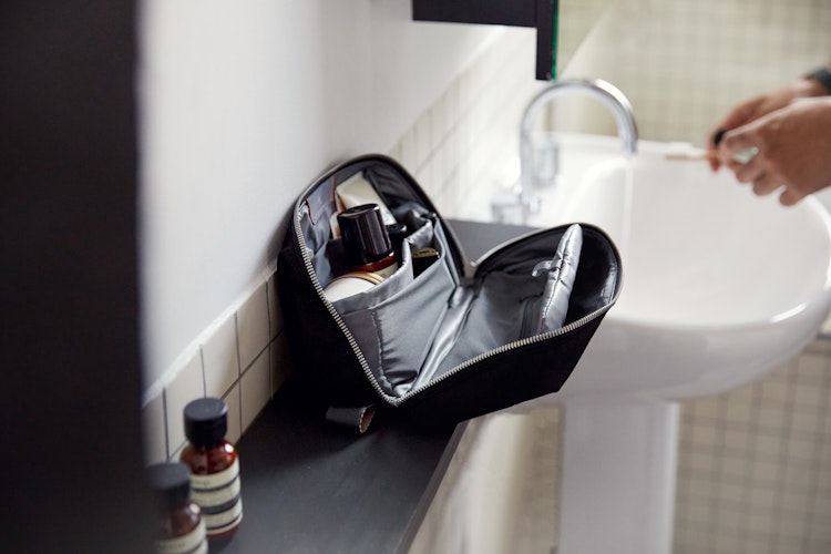 Bellroy Toiletry Kit Plus in black nylon, displayed open on a bathroom shelf, with organized interior and personal items in use.