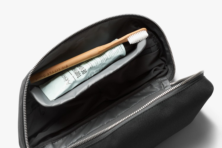 Open black Bellroy Toiletry Kit Plus displayed with a bamboo toothbrush and toothpaste, highlighting its slate gray interior details.