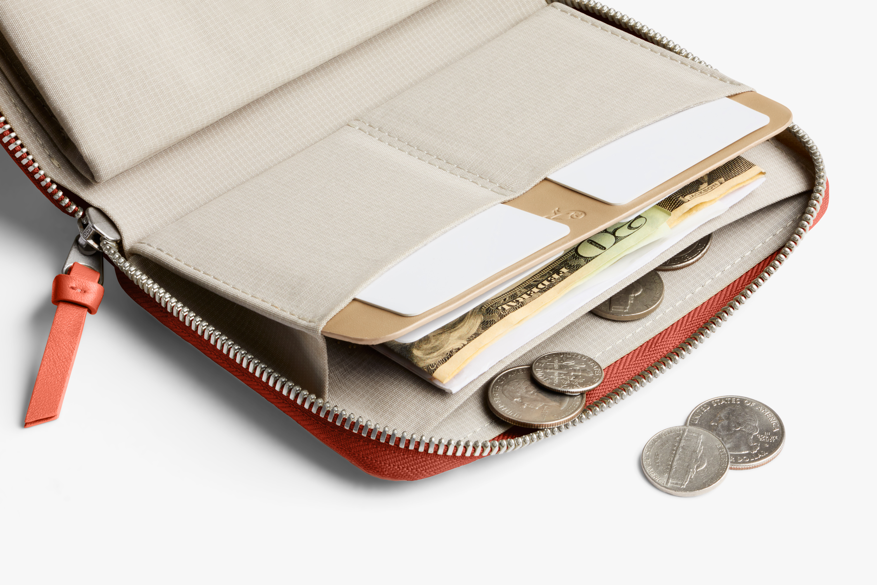 Bellroy Folio Wallet opens to reveal compartments for cash, cards and coins; additional coins on the white surface emphasize storage capacity.