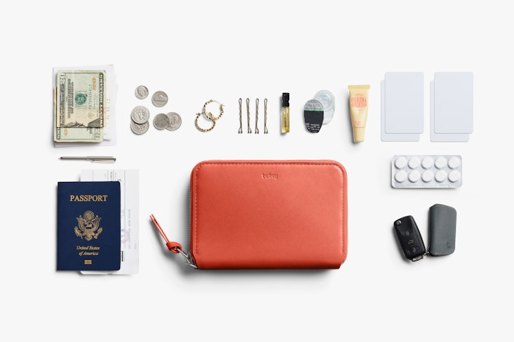 Bellroy Folio Wallet in blood orange leather with RFID, shown open with travel items and accessories arranged on a white background.