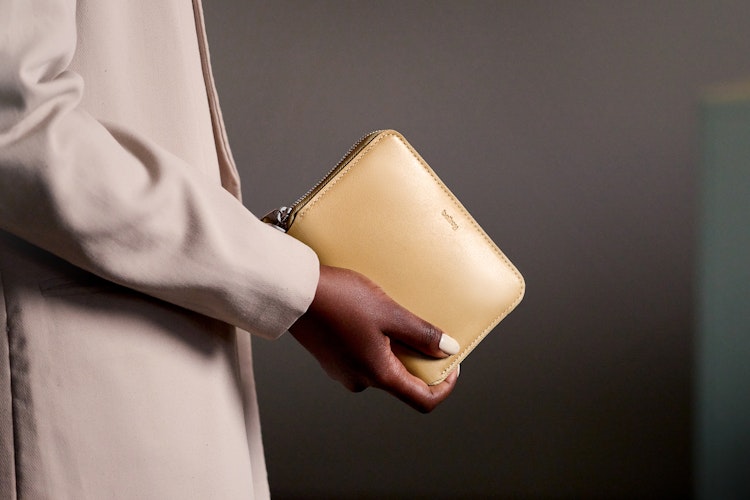 A person in a light-colored jacket holds the Bellroy Folio Wallet, an elegant black leather RFID wallet, in front of a plain background.