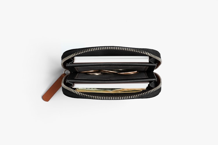 The Bellroy Folio Mini RFID wallet made of black leather is displayed on a white background with blank cards, stacked bills and coins.