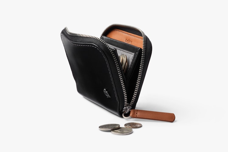 The Bellroy Folio Mini wallet with RFID zipper made of black leather is partially open and shows cash and a white card on a white background.