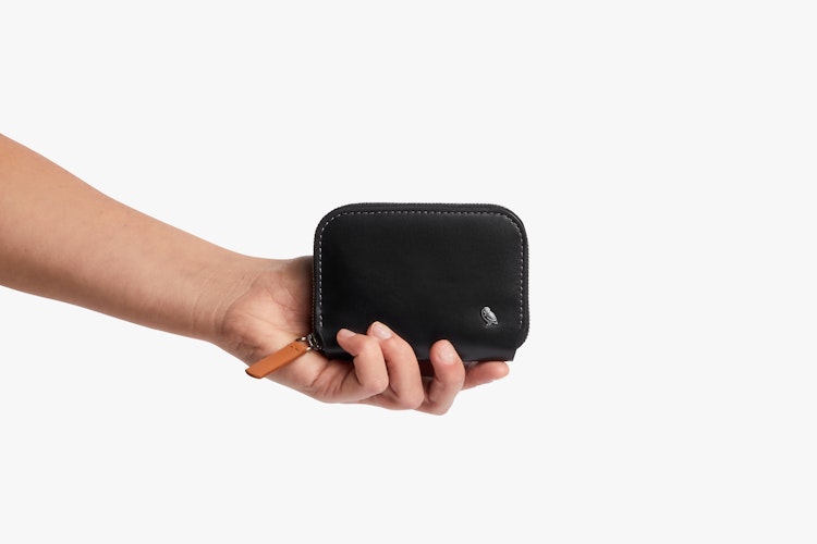The Bellroy Folio Mini RFID wallet made of black leather, with silver zipper, brown pull tab and logo on a white background.