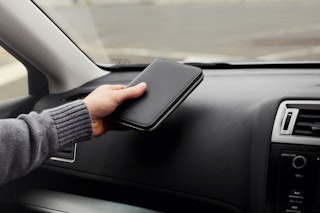 A person in a gray sweater sets the black leather Bellroy Travel Folio RFID wallet on a car dashboard, highlighting its sleek design.