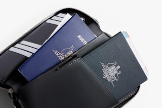 Bellroy Beautifully presented black travel folio opens to reveal two passports and a boarding pass, neatly arranged on a white background .