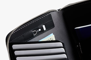 Close-up of Bellroy Travel Folio’s black leather interior with card slots, cards, folded bills, and a dark booklet on the right.