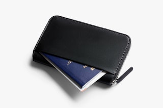 Bellroy Travel Folio Black leather wallet with zipper, opened with a passport inside, with RFID protection on a white surface.