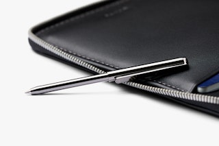 Bellroy Travel Folio with black leather RFID zip case, silver pen placed on top, and a blue card partially visible inside.