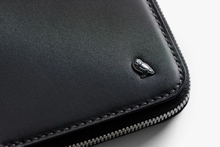 Close-up of the Bellroy Travel Folio, a black leather RFID wallet with zipper closure, textured finish, clean stitching and metallic owl logo.