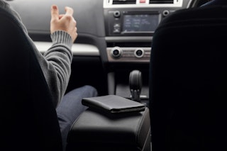 Closed black Bellroy Travel Folio on the center armrest of a car, showing off its sleek design and practicality when traveling.
